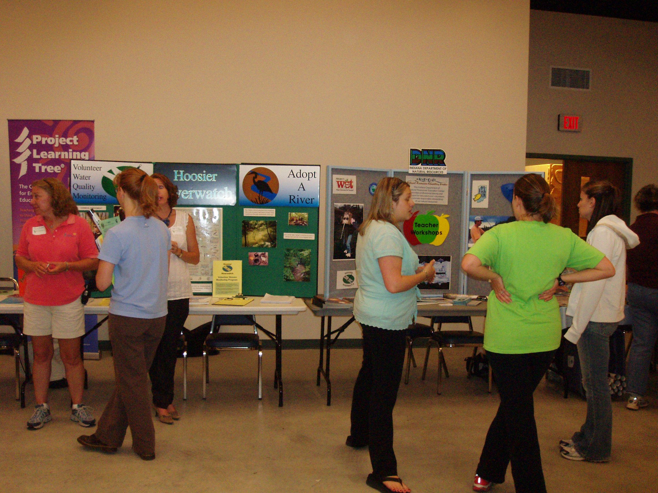Group of people interacting at a community event with various informational displays on tables.