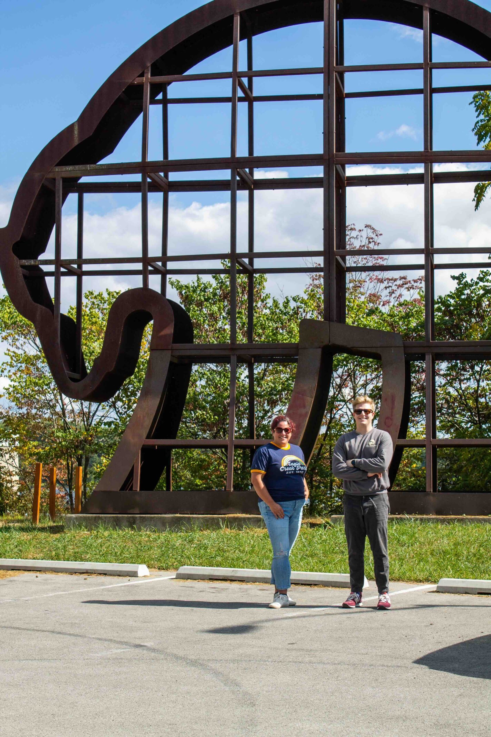 Two individuals standing in front of a large metal sculpture resembling an elephant's head at Bear Overlook.